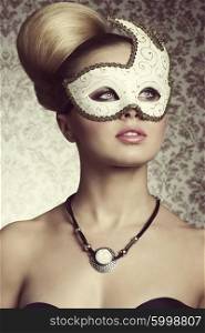 Stunning blonde lady with elegant hair-style and romantic eyes posing with decorated mask on her visage and stylish necklace.