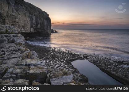 Stunning coastal landscape with long exposure waves crashing onto rocks at sunrise