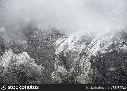 Stunning dramatic landscape image of snowcapped Glyders mountain range in Snowdonia during Winter with menacing low clouds hanging at the mountain peaks