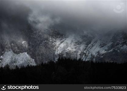 Stunning dramatic landscape image of snowcapped Glyders mountain range in Snowdonia during Winter with menacing low clouds hanging at the mountain peaks