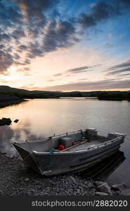 Stunning dramatic sunrise over calm lake with boat on shore