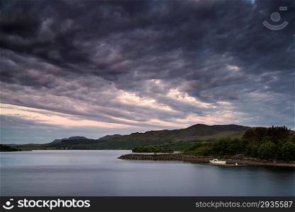 Stunning dramatic sunrise over calm lake with boat on shore
