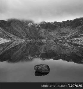 Stunning dramatic Winter landscape image of Llyn Idwal and snowcapped Glyders Mountain Range in Snowdonia in black and white