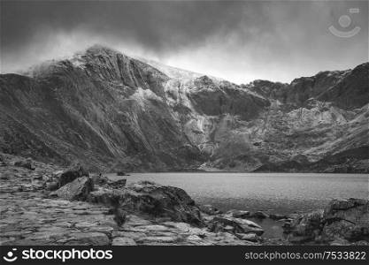 Stunning dramatic Winter landscape image of Llyn Idwal and snowcapped Glyders Mountain Range in Snowdonia in black and white