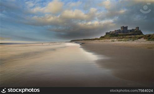 Stunning epic sunrise landscape over beach with medieval castle ruins in background