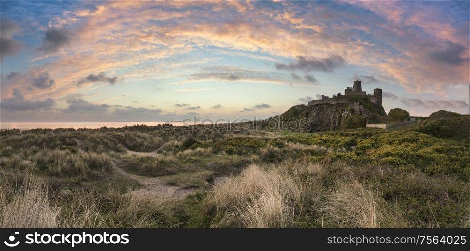 Stunning epic sunrise landscape over beach with medieval castle ruins in background