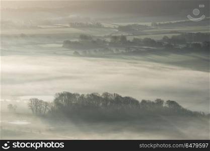 Stunning foggy English rural landscape at sunrise in Winter with. Beautiful foggy English countryside landscape at sunrise in Winter with layers rolling through the fields