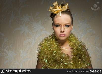 stunning girl with freckles posing with shiny artistic christmas make-up, sparkle tinsel around neck and golden ribbon on hair-style. Looking in camera with charming expression