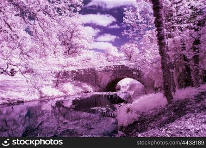 Stunning infra red landscape image of old bridge over river in countryside