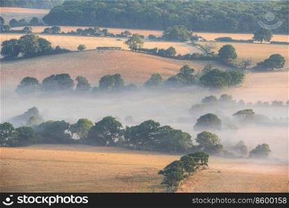 Stunning landscape ima≥of layers of mist rolling over South Downs National Park English countryside during misty Summer sunrise