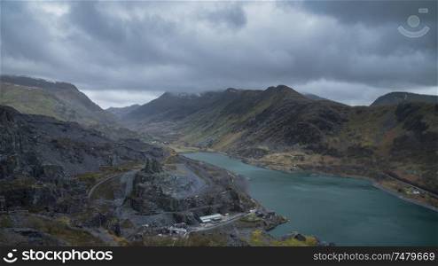 Stunning landscape image of Dinorwig Slate Mine and snowcapped Snowdon mountain in background during Winter in Snowdonia with Llyn Peris in foreground