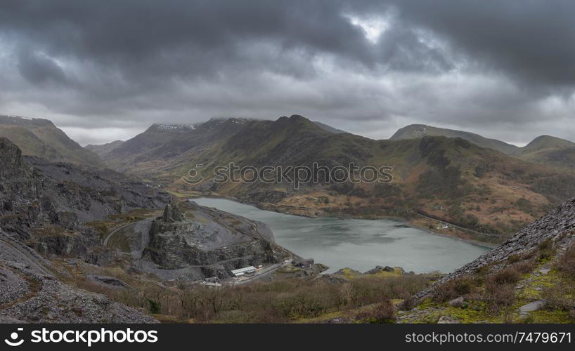 Stunning landscape image of Dinorwig Slate Mine and snowcapped Snowdon mountain in background during Winter in Snowdonia with Llyn Peris in foreground