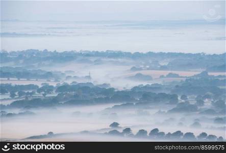 Stunning landscape image of layers of mist rolling over South Downs National Park English countryside during misty Summer sunrise