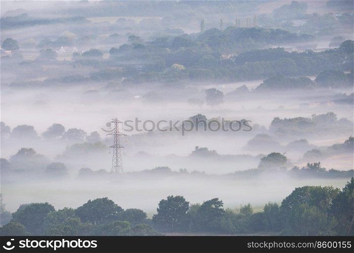 Stunning landscape image of layers of mist rolling over South Downs National Park English countryside during misty Summer sunrise