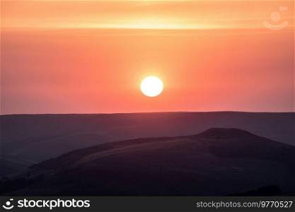 Stunning late Summer sunset landscape image of setting sun kissing the horizon in the Peak District, viewed from Higger Tor