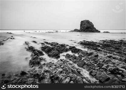 Stunning long exposure landscape image of sea over rocks during sunset in black and white