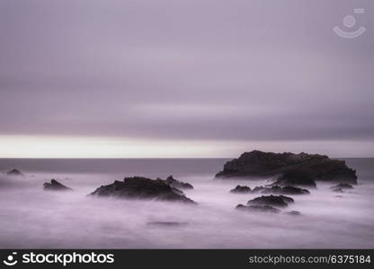 Stunning long exposure landscape image of sea over rocks during vibrant sunset