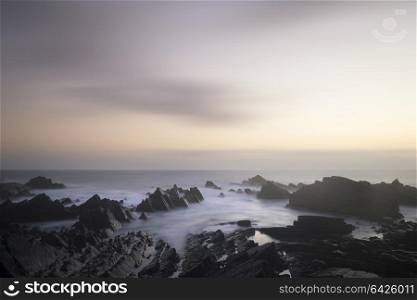 Stunning long exposure landscape image of sea over rocks during vibrant sunset