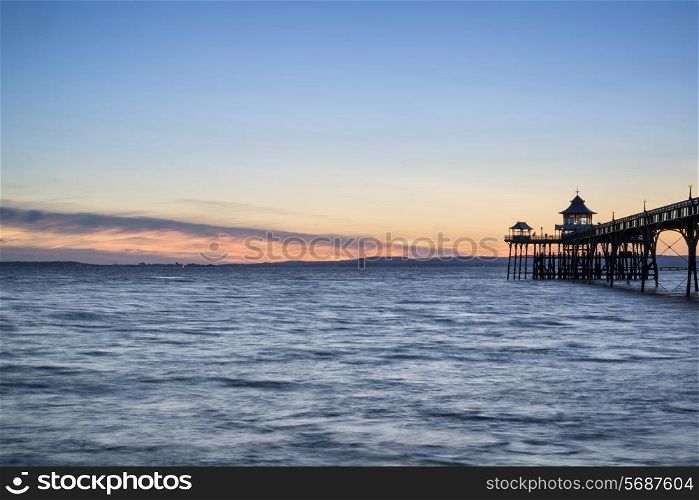 Stunning long exposure sunset over ocean with pier silhouette