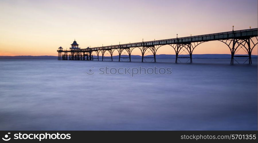 Stunning long exposure sunset over ocean with pier silhouette