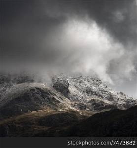 Stunning moody dramatic Winter landscape image of snowcapped Tryfan mountain in Snowdonia during stormy weather