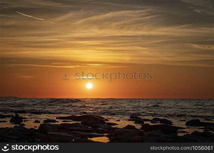 Stunning morning seascape with sun and stones on the water