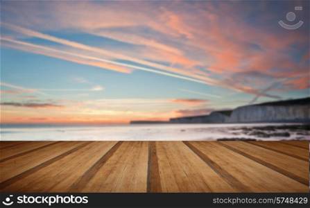 Stunning Summerr sunset over ocean with cliffs, rocks and vibrant colors with wooden planks floor