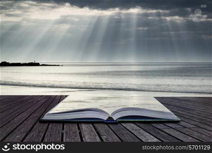 Stunning sun beams bursting from sky over empty yellow sand beach landscape conceptual book image
