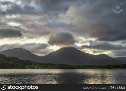 Stunning sunrise landscape image looking across Loweswater in the Lake District towards Low Fell and Grasmere with colorful sky breaking on the mountain peaks