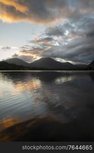 Stunning sunrise landscape image looking across Loweswater in the Lake District towards Low Fell and Grasmere with colorful sky breaking on the mountain peaks