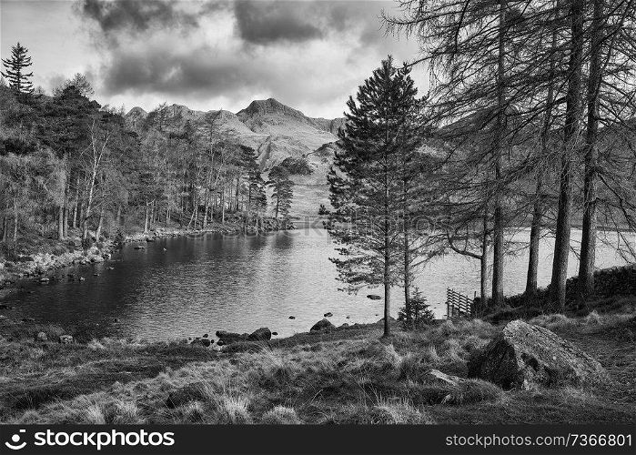 Stunning sunrise landscape image of Blea Tarn in UK Lake District with Langdales Range in background in black and white