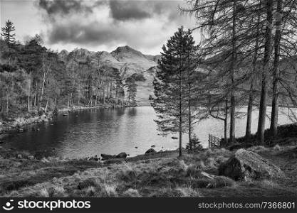 Stunning sunrise landscape image of Blea Tarn in UK Lake District with Langdales Range in background in black and white