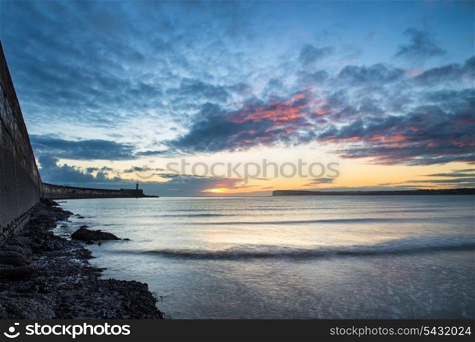 Stunning sunrise over ocean with lighthouse and harbor wall