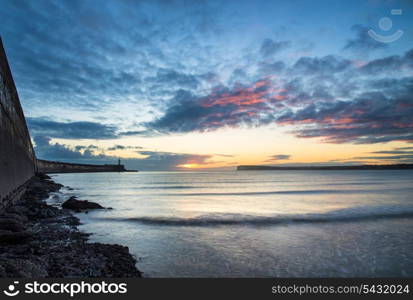 Stunning sunrise over ocean with lighthouse and harbor wall