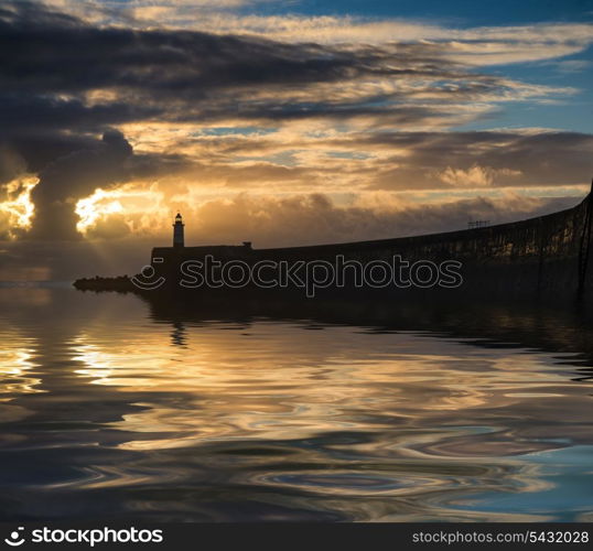 Stunning sunrise over ocean with lighthouse and harbor wall