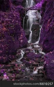 Stunning surreal alternative color tall waterfall flowing over lush green landscape foliage in early Autumn
