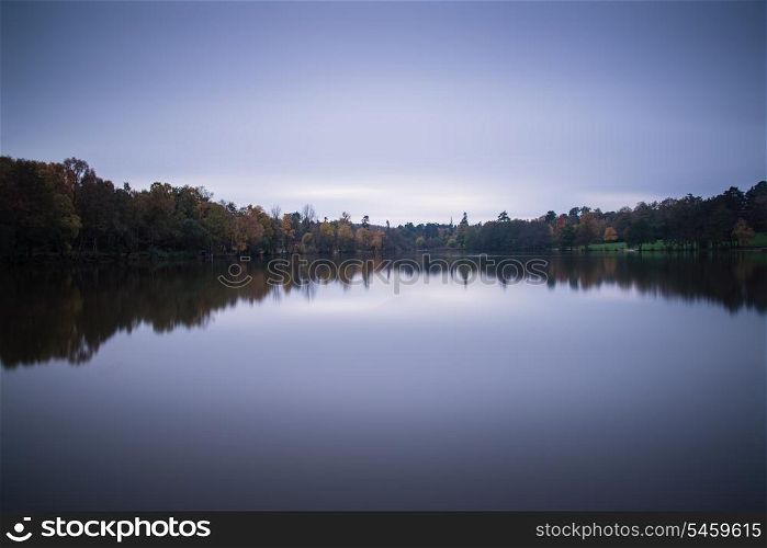 Stunning vibrant Autumn woodland reflected in still lake water during twilight landscape