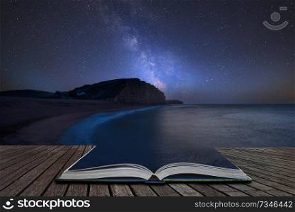 Stunning vibrant Milky Way composite image over landscape of long exposure of West Bay in Dorset coming out of pages in magical story book