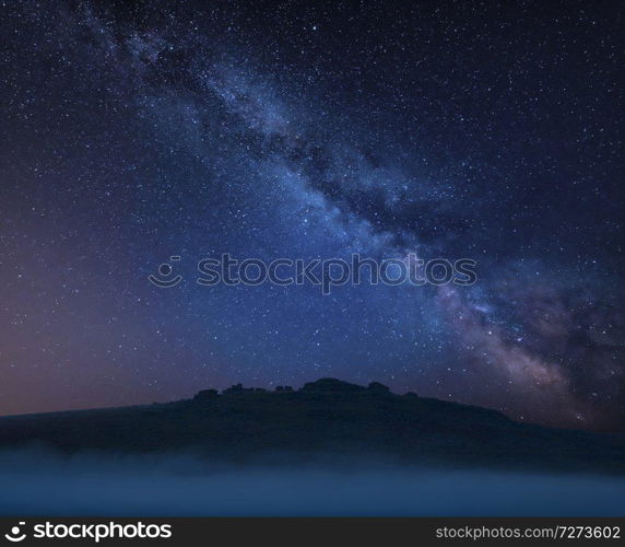 Stunning vibrant Milky Way composite landscape image over the tors in Dartmoor revealing peaks through the mist