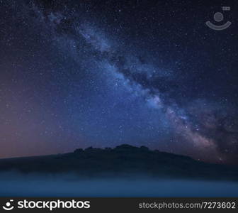 Stunning vibrant Milky Way composite landscape image over the tors in Dartmoor revealing peaks through the mist