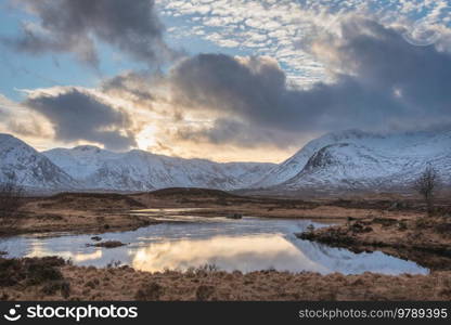 Stunning Winter panorama landscape image of mountain range viewed from Loch Ba in Scottish Highlands with dramatic clouds overhead