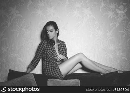 stunning woman in sexy pose on backrest of sofa with unbuttoned plaid shirt and nude legs.black and white image&#xA;