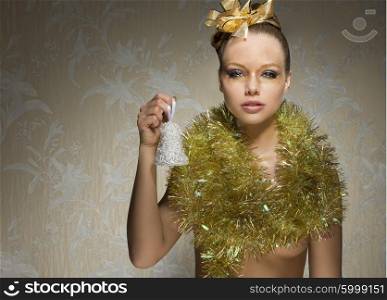 stunning woman with freckles posing in artistic christmas shoot with little bell in the hand, golden ribbon in the hair-style, christmas glossy make-up and shiny tinsel around neck.