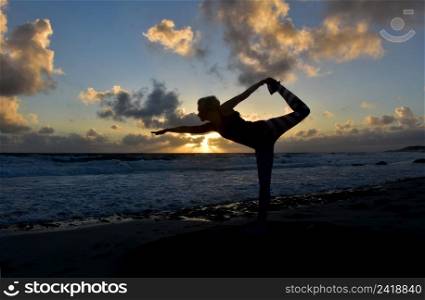 Stunning yoga dancer pose silhouetted at sunrise along the coast.