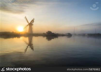 Stunnnig landscape of windmill and river at sunrise on Summer morning