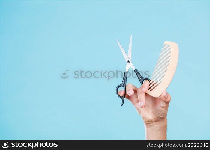 Style and fashion. Male hand of hairstylist barber holds scissors and wooden comb, creating hairdo coiffure. Male hand with scissors and comb