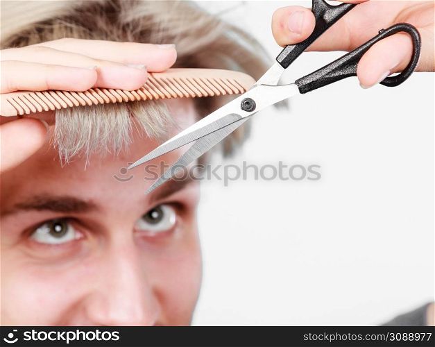 Style and fashion. Young trendy male hairstylist barber with new idea of look changing. Blonde guy with scissors and comb creating coiffure cutting his bangs.. Man with scissors and comb creating new coiffure