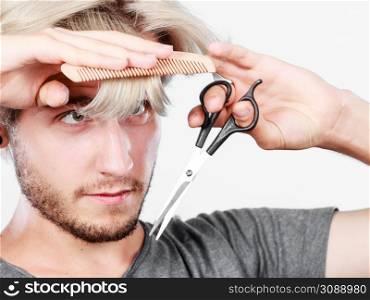 Style and fashion. Young trendy male hairstylist barber with new idea of look changing. Blonde guy with scissors and comb creating coiffure cutting his bangs.. Man with scissors and comb creating new coiffure