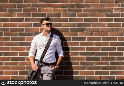 style and people concept - young man in sunglasses with bag over brickwall. young man in sunglasses with bag over brickwall