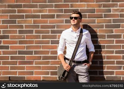 style and people concept - young man in sunglasses with bag over brickwall. young man in sunglasses with bag over brickwall